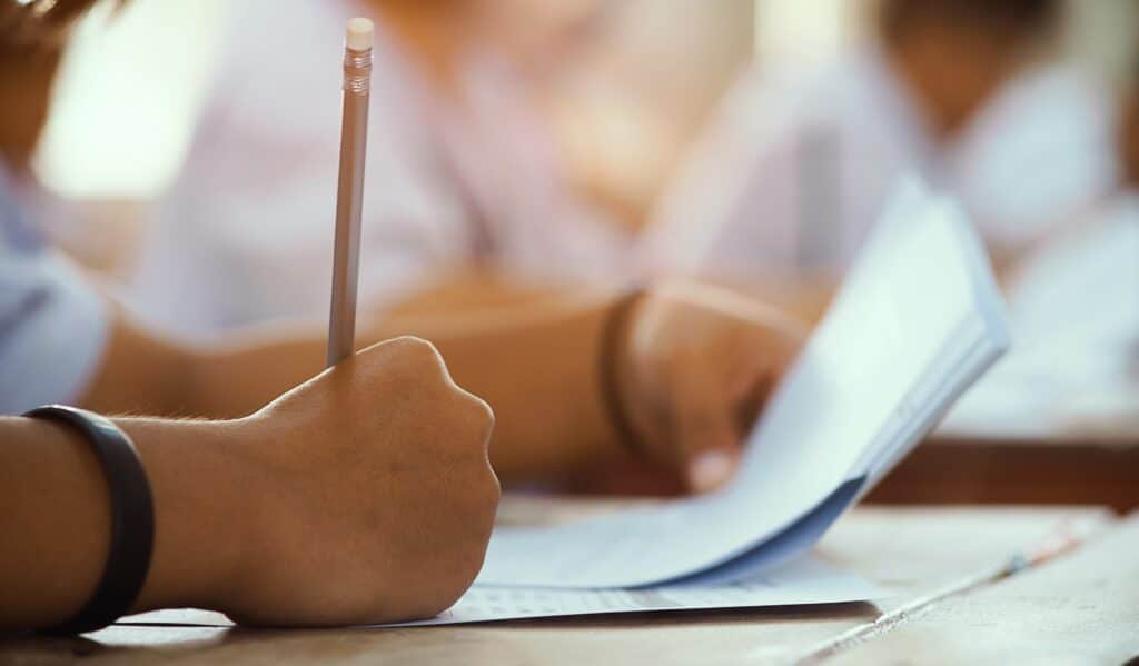 Closeup to hand of student  holding pencil and taking exam in classroom with stress for education test.