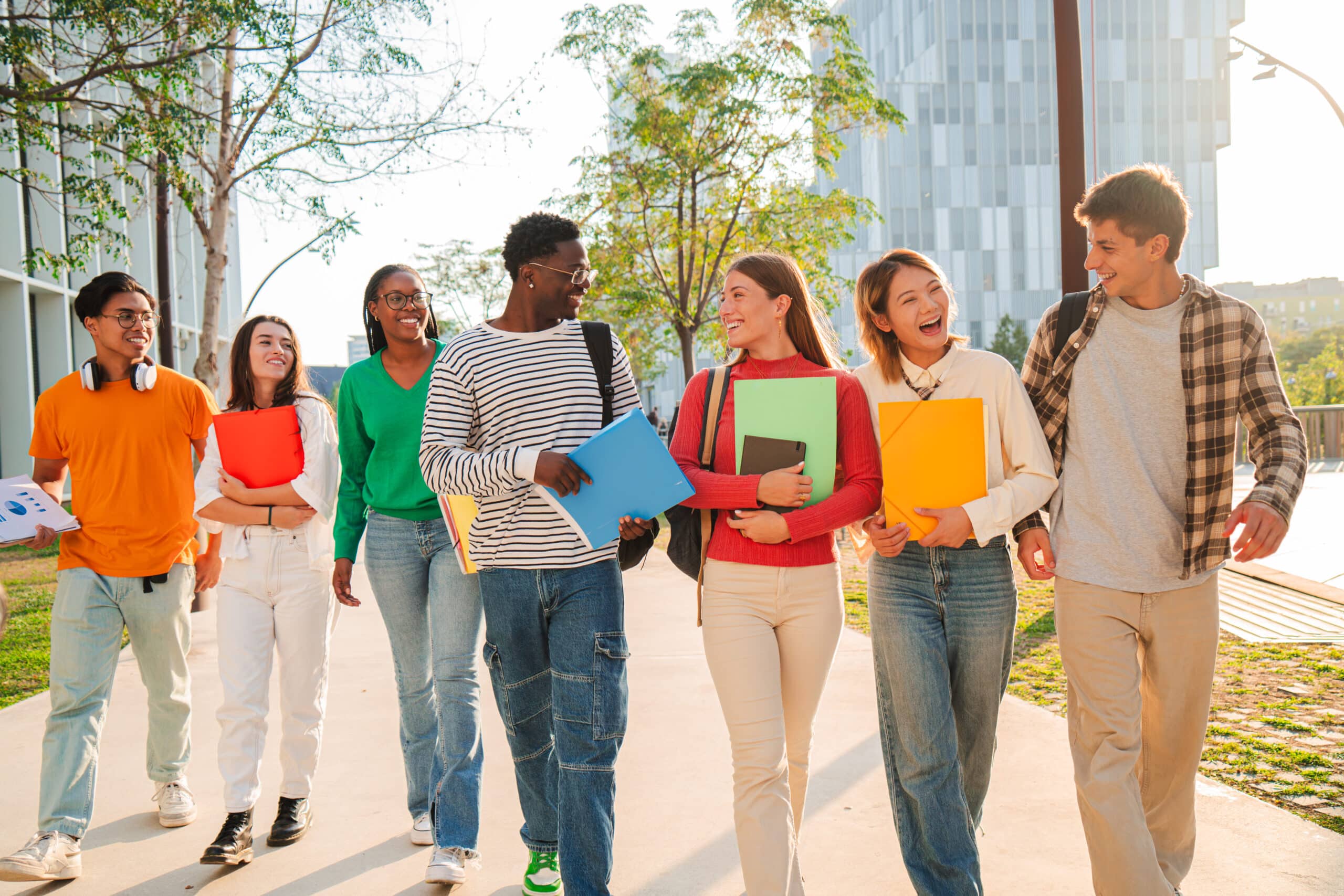 Big group of international classmates walking and talking together on the university campus. Happy multiethnic students laughing while going to academy class. Young mates chatting back to high school. High quality photo