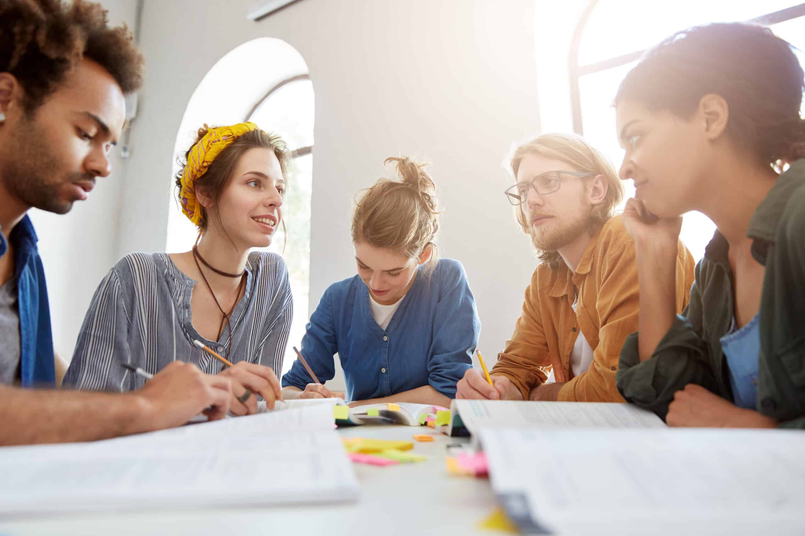 Young college students from different countries working together sitting at coworking space at table discussing main issues presenting their knowledge in particular sphere exchanging expreience
